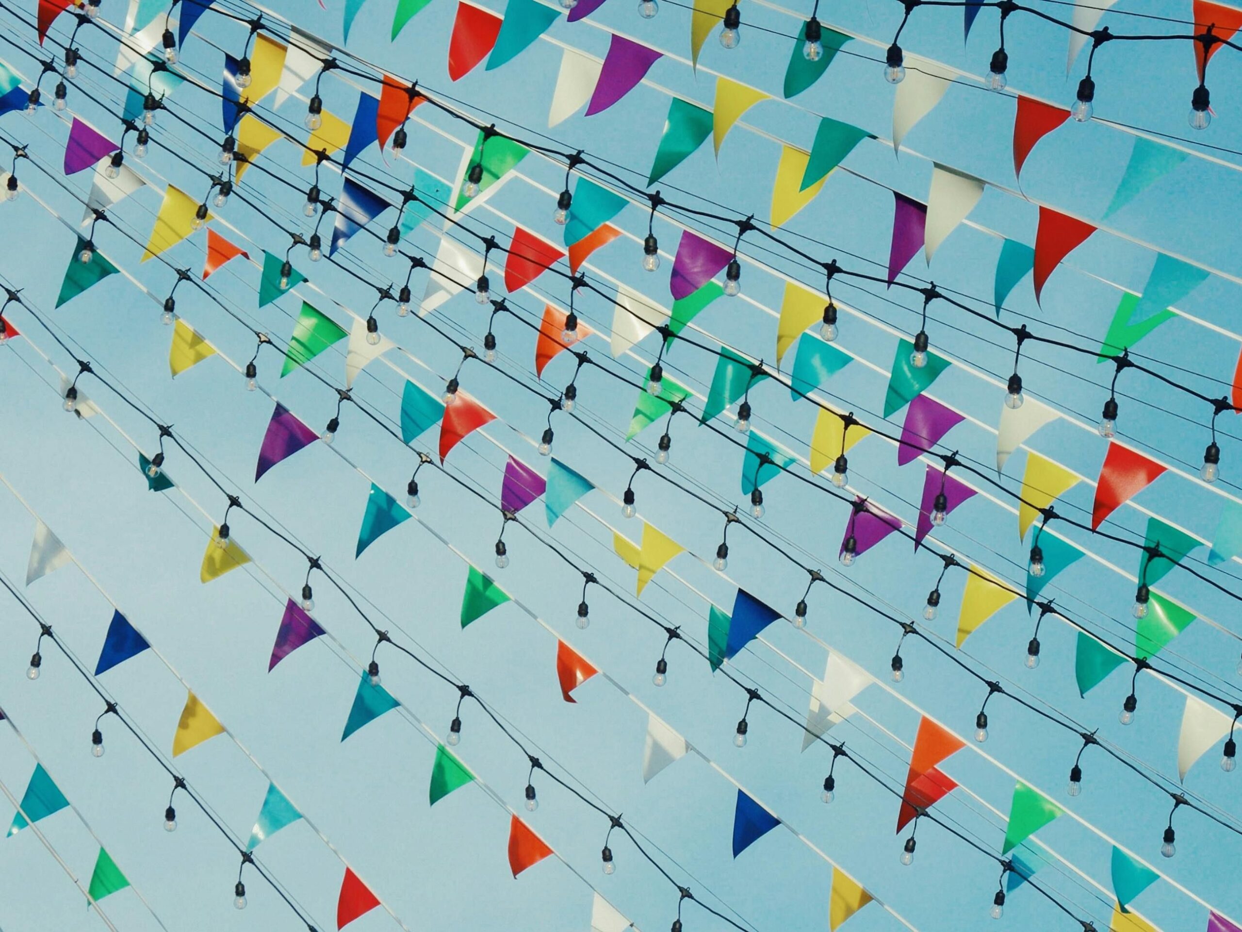 Colorful triangular bunting and lights hung outdoors on a sunny day.