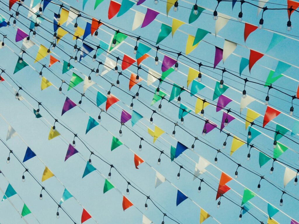 Colorful triangular bunting and lights hung outdoors on a sunny day.